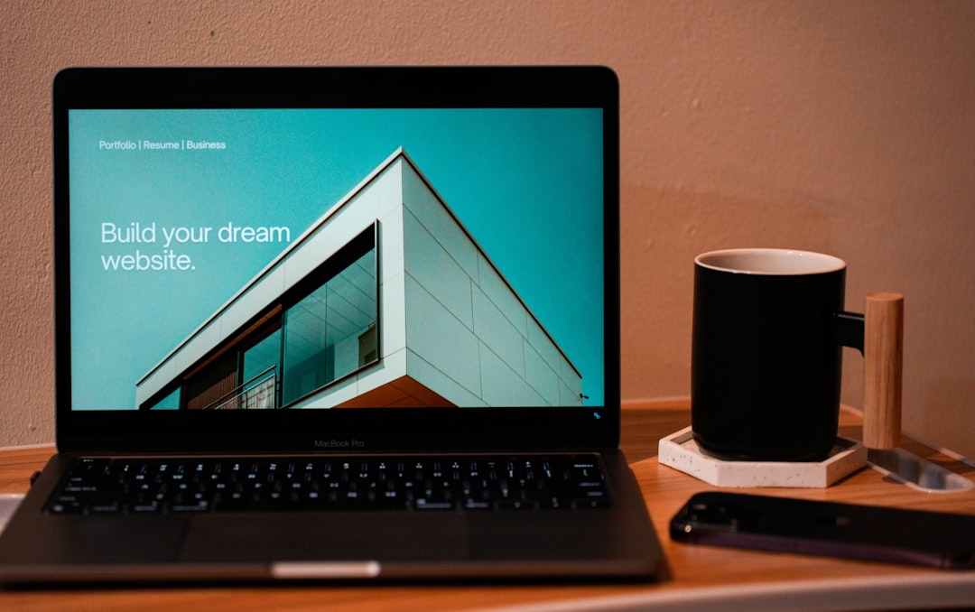 Create the website of your dreams for what lies ahead. A laptop, MacBook, resting on a portable table with a coffee tea mug beside it.